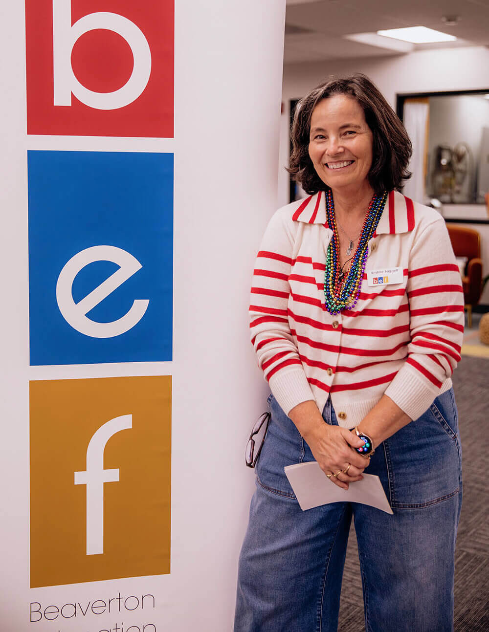 Kristine Baggett standing in front of a Beaverton Education Foundation sign, where she served as Executive Director for close to 20 years